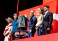 Five People Stand on a Red Fifa World Cup Stage, One Holding a Dark Gray Shirt with Sponsor Logos for Display. - Entre Regios