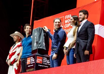 719771216_1528499245956813_2134603666955572734_n - Entre Regios Five People Stand on a Red Fifa World Cup Stage, One Holding a Dark Gray Shirt with Sponsor Logos for Display. - Entre Regios