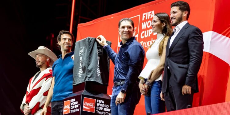 Five People Stand on a Red Fifa World Cup Stage, One Holding a Dark Gray Shirt with Sponsor Logos for Display. - Entre Regios