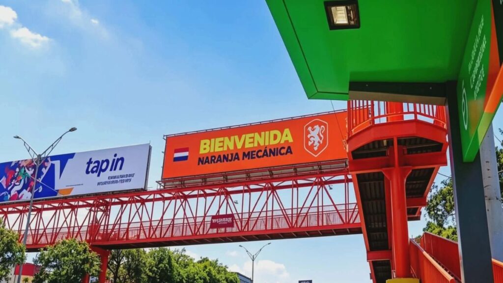 Bright Orange 'bienvenida Naranja MecÁnica' Sign with a Crest on a Red Elevated Pedestrian Bridge Under a Blue Sky. - Entre Regios