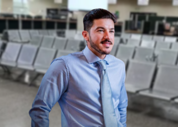 Man in a Light Blue Dress Shirt and Patterned Tie Stands in a Spacious Waiting Area with Rows of Gray Chairs Behind Him, Looking off to the Side. - Entre Regios