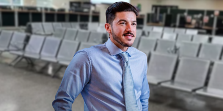 Man in a Light Blue Dress Shirt and Patterned Tie Stands in a Spacious Waiting Area with Rows of Gray Chairs Behind Him, Looking off to the Side. - Entre Regios