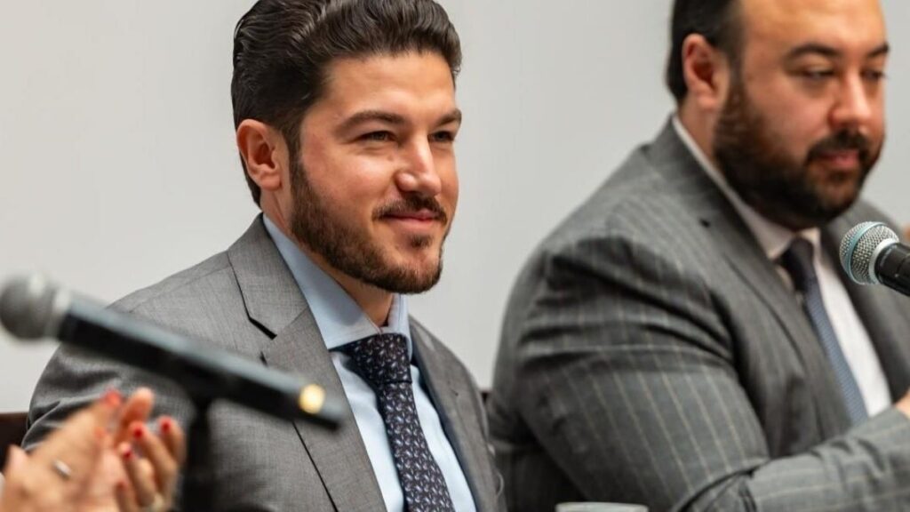 Two Panelists in Gray Business Suits Speaking into Microphones During a Discussion; Man on Left Smiles Slightly While the Other is Blurred in the Background - Entre Regios